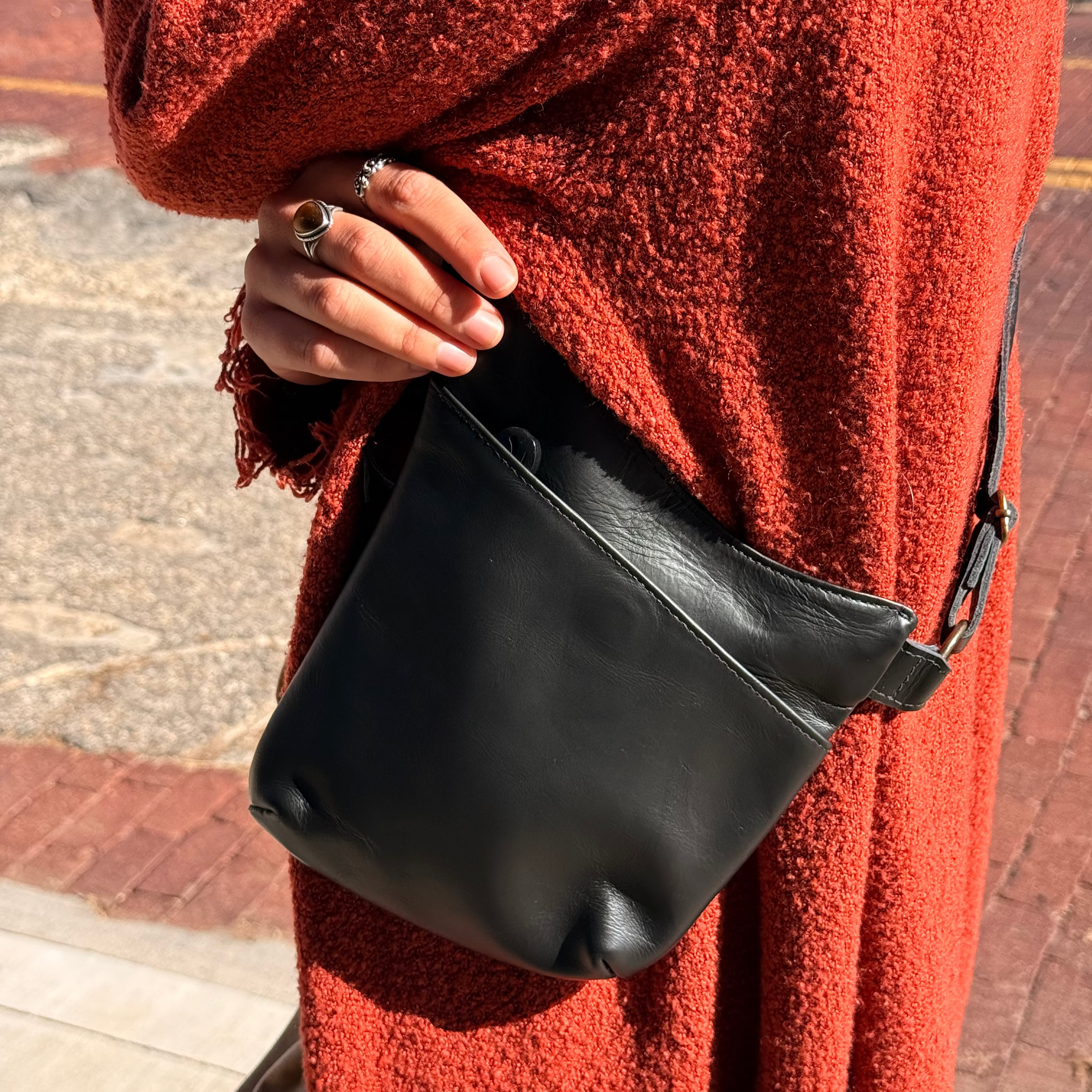 Person wearing a red coat holding a black leather bag on a brick pavement.