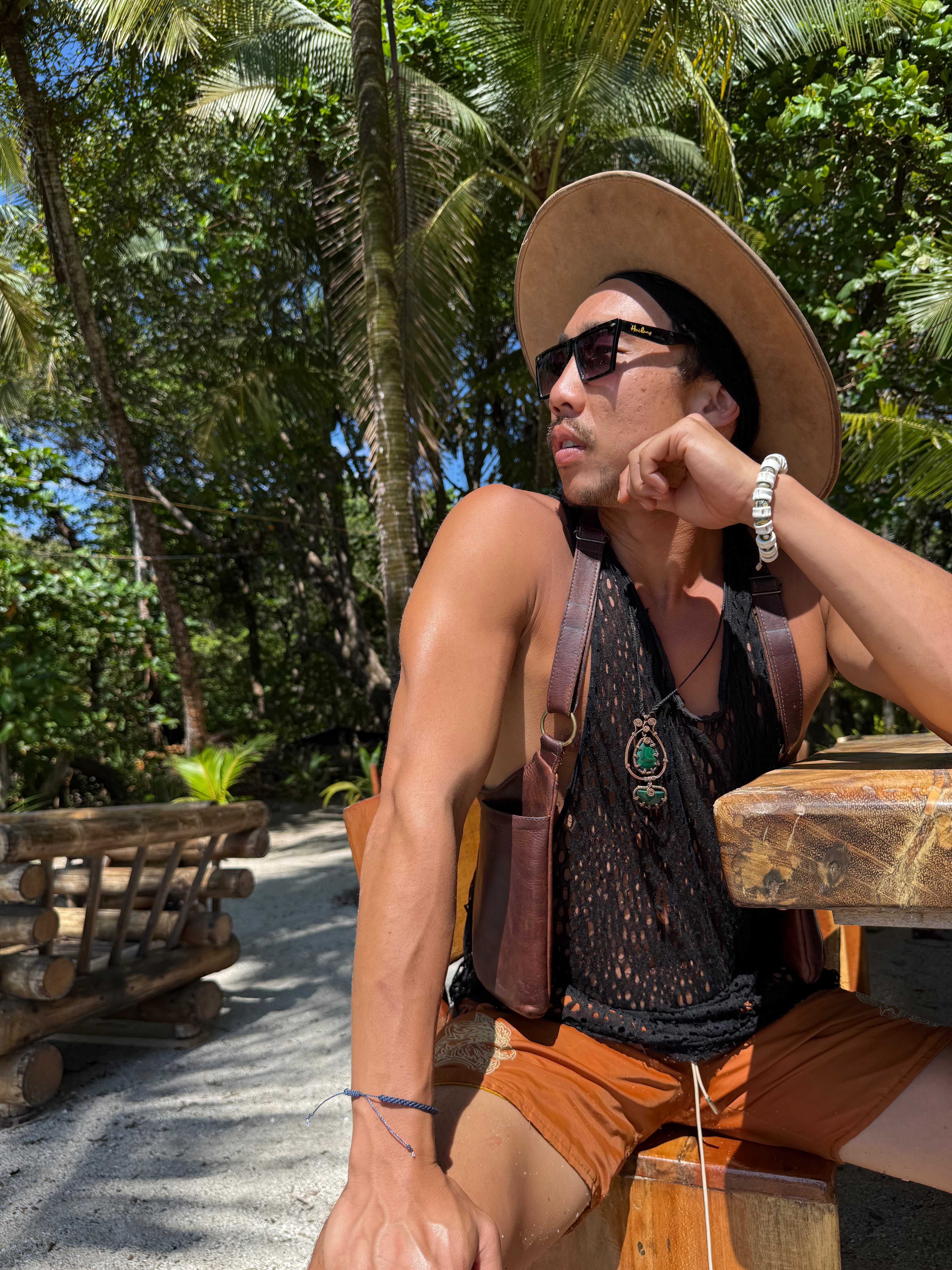 Man wearing a straw hat and sunglasses sitting outdoors with palm trees in the background with leather handbag, mens leather handbag, unisex leather handbag burning man 